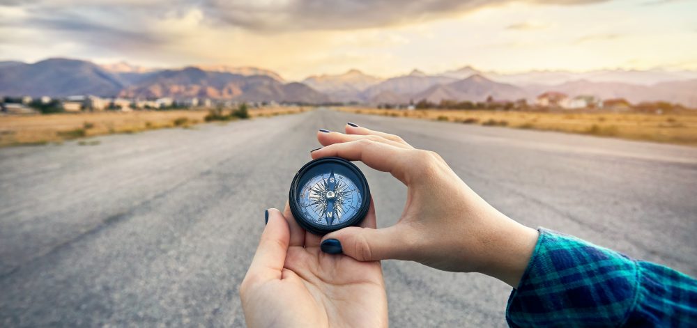 Woman hands in green shirt holding compass at sunrise sky background. Travel and adventure concept.